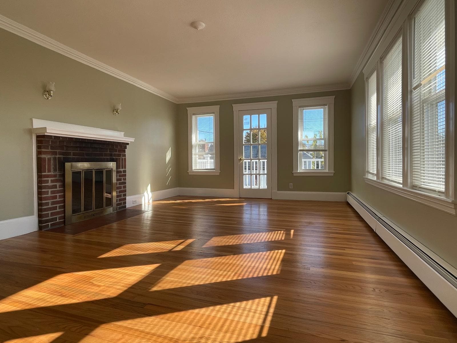 Sun-drenched living room with brick fireplace and hardwood floors